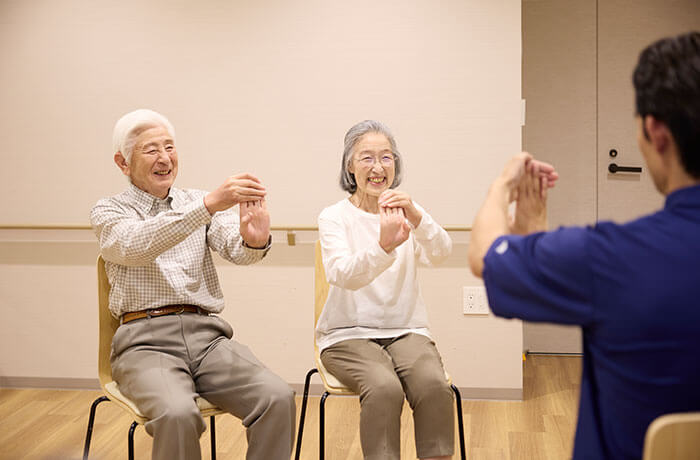介護施設でのレクリエーション。高齢者2名が職員と一緒に楽しく身体活動を行っている